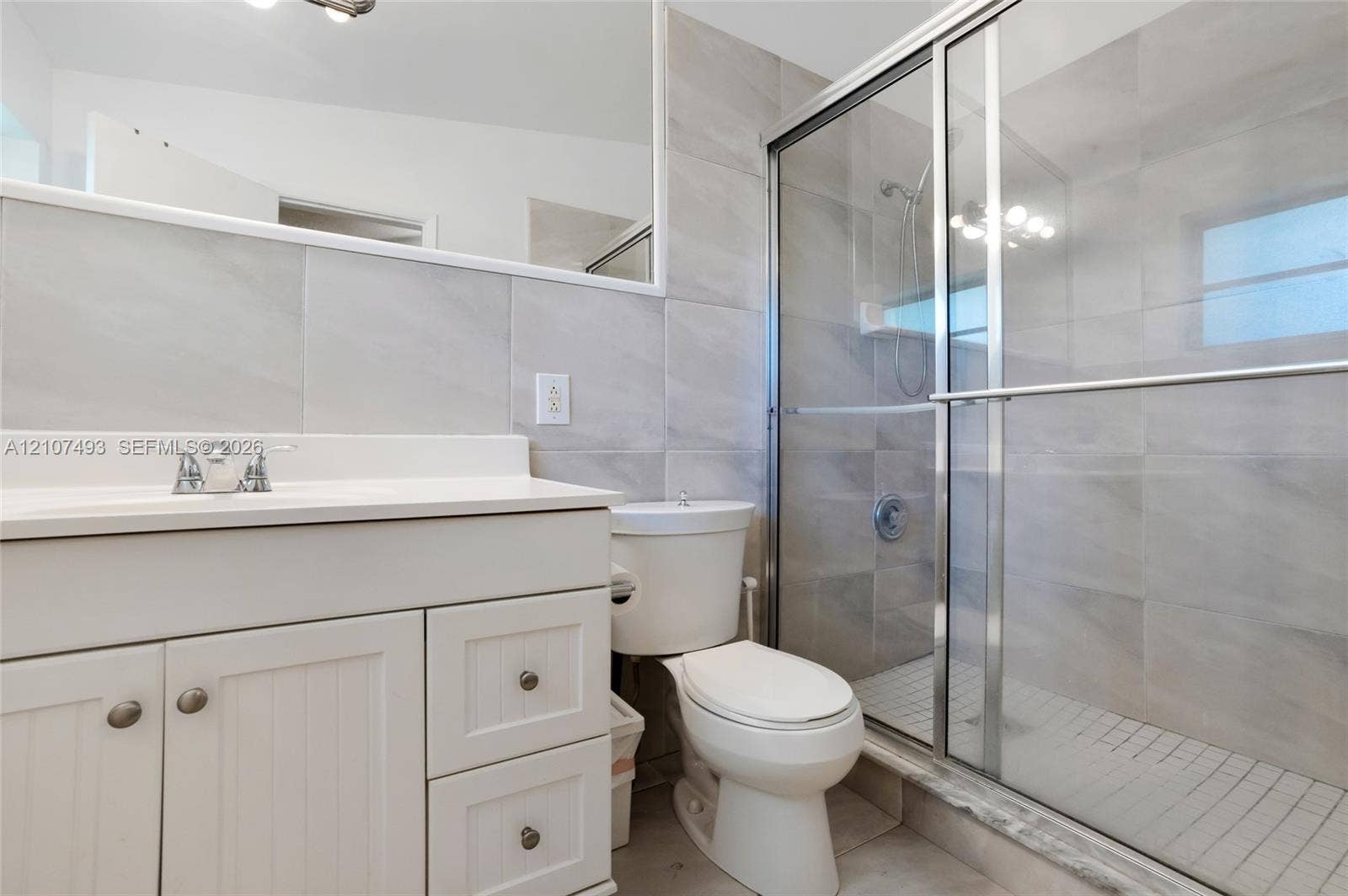 2645 NE 32nd Street, Fort Lauderdale, FL 33306 Bathroom featuring a white vanity cabinet, large wall-mounted mirror, walk-in shower with sliding glass doors, and light-toned tile wall finishes