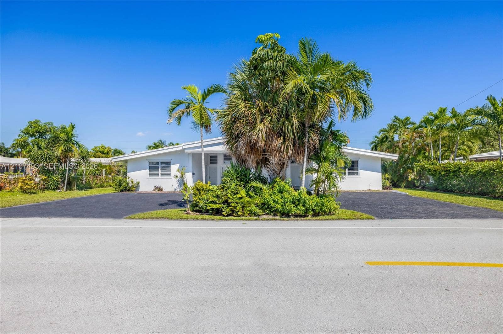 2645 NE 32nd Street, Fort Lauderdale, FL 33306 Single-story residence featuring a white exterior, expansive asphalt driveway, and mature landscaping