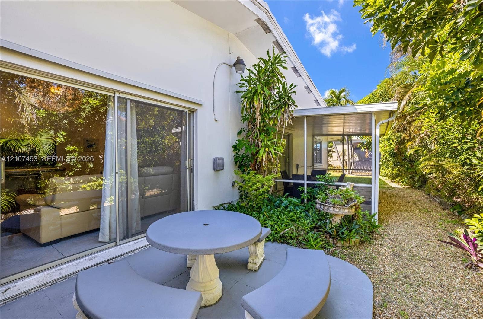 2645 NE 32nd Street, Fort Lauderdale, FL 33306 Exterior patio featuring a concrete dining table with curved benches, sliding glass doors, and a screened-in lanai