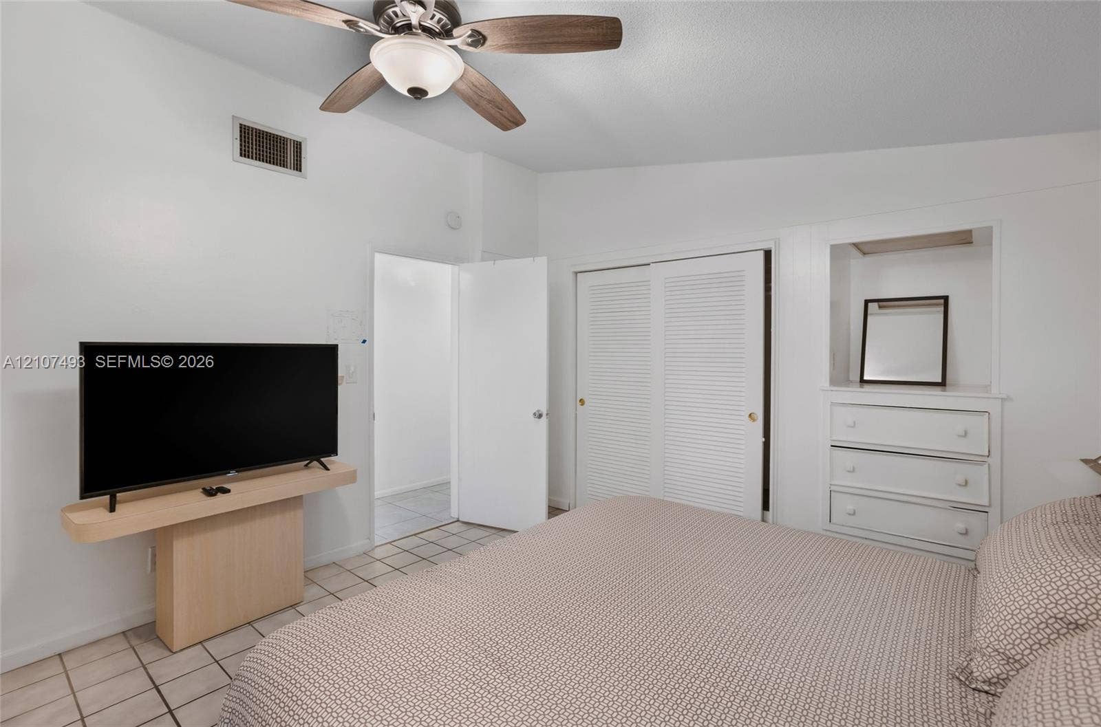 2645 NE 32nd Street, Fort Lauderdale, FL 33306 Room featuring vaulted ceilings, neutral ceramic tile flooring, ceiling fan with integrated lighting, built-in wooden shelving, and a closet with louvered doors