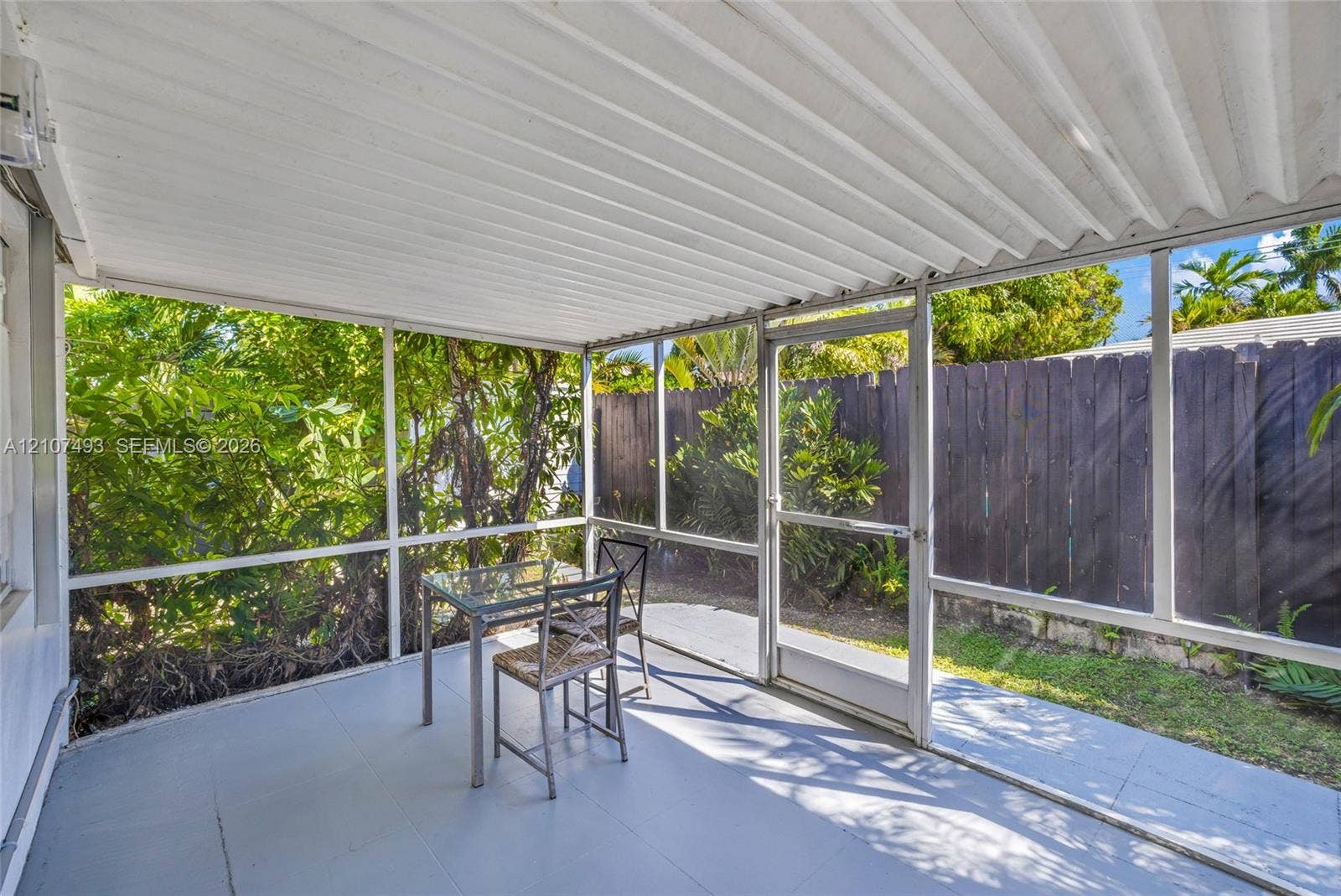 2645 NE 32nd Street, Fort Lauderdale, FL 33306 Screened-in porch featuring a corrugated metal roof, aluminum framing, solid flooring, and a private wooden fence perimeter