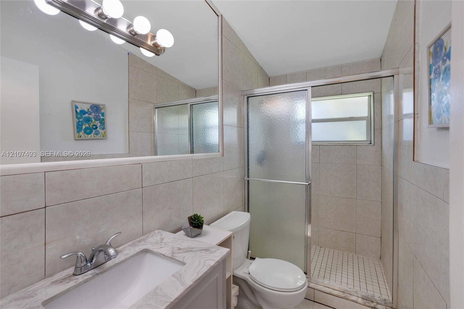 2645 NE 32nd Street, Fort Lauderdale, FL 33306 Bathroom featuring a stone-finish countertop, undermount sink, full-width vanity mirror, six-light fixture, and a tiled shower enclosure with sliding glass doors