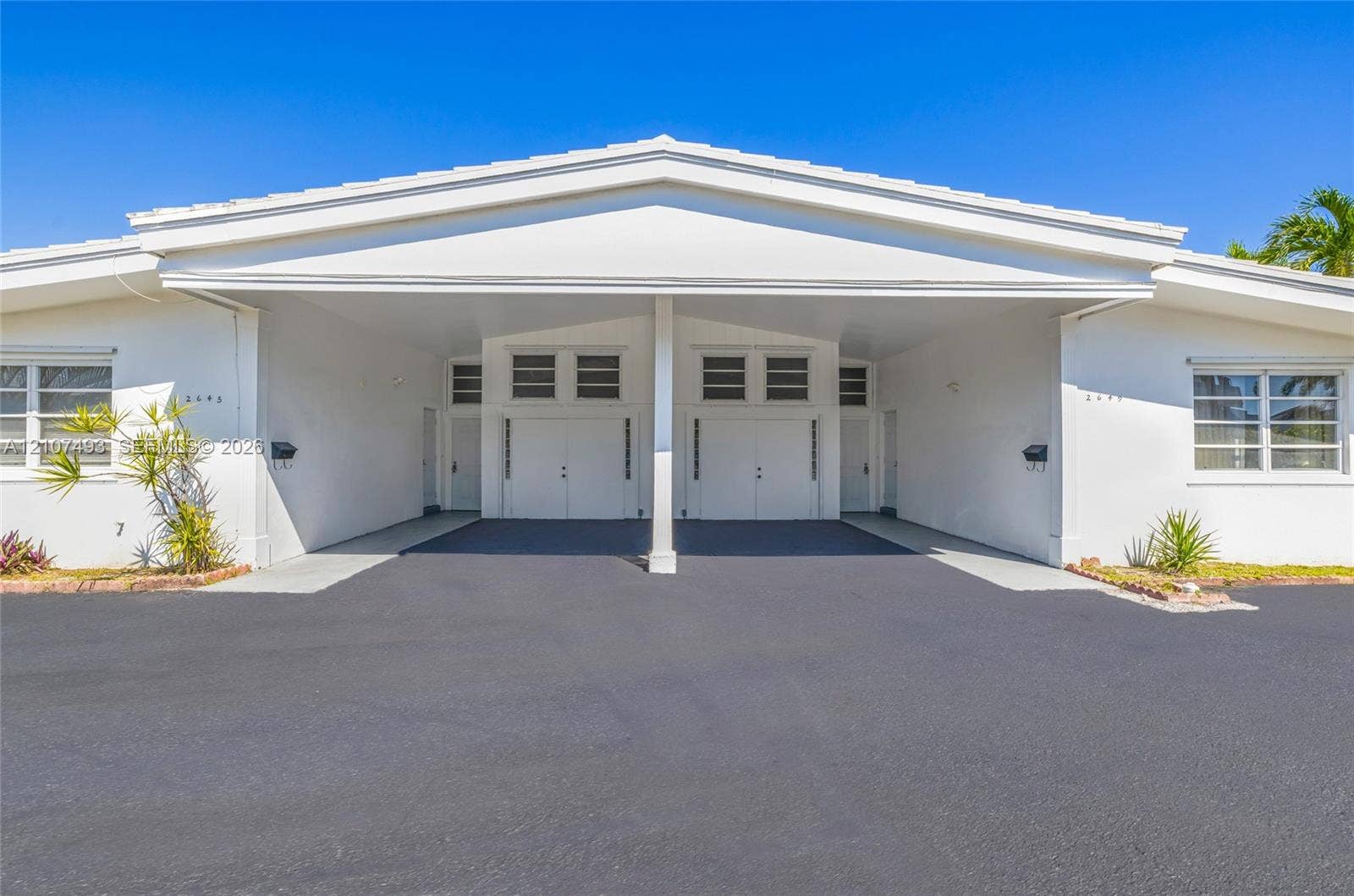 2645 NE 32nd Street, Fort Lauderdale, FL 33306 Single-story exterior featuring white stucco siding, a covered central carport, multi-pane windows, and glass block accents