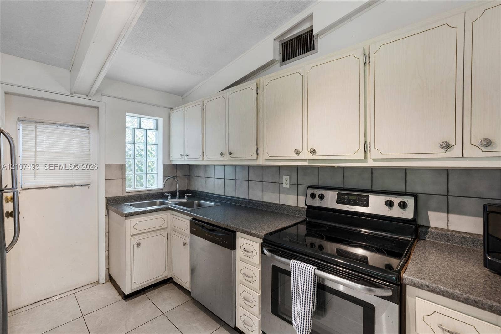 2645 NE 32nd Street, Fort Lauderdale, FL 33306 Kitchen featuring white cabinetry, dark stone-finish countertops, stainless steel appliances, a square glass block window, and tile flooring