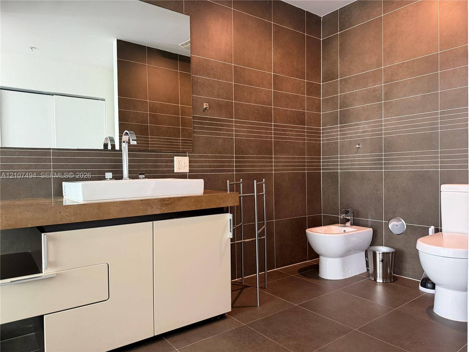 2100 Park Avenue, #305, Miami Beach, Miami Beach, FL 33139 Wall-to-wall brown ceramic tile, custom white vanity with a rectangular vessel sink, polished chrome fixtures, integrated bidet, and large-format wall mirror