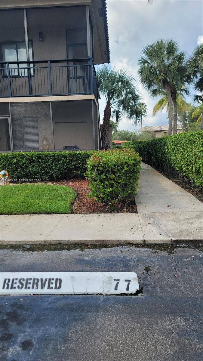 330 Racquet Club Road, #204, Weston, Weston, FL 33326 Two-story structure featuring a screened balcony with dark metal railings, concrete walkway, manicured hedging, and designated reserved parking space