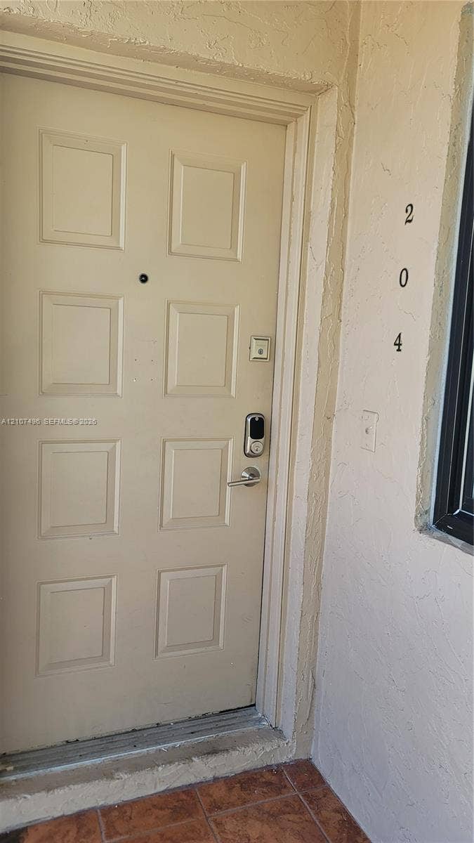 330 Racquet Club Road, #204, Weston, Weston, FL 33326 Eight-panel entry door featuring a digital smart lock, integrated peephole, and metallic lever handle, set against textured stucco exterior walls and tile flooring