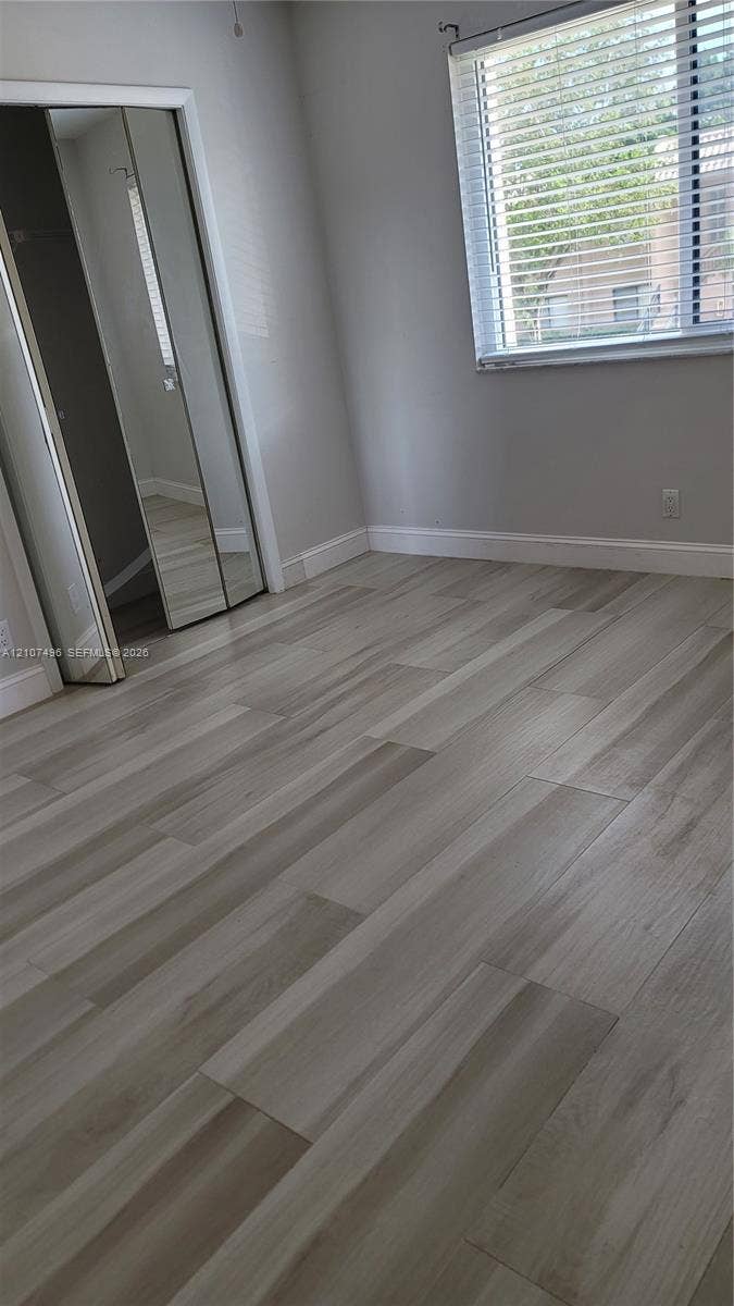 330 Racquet Club Road, #204, Weston, Weston, FL 33326 Neutral-toned wood-finish flooring, mirrored closet doors, and a window with horizontal blinds