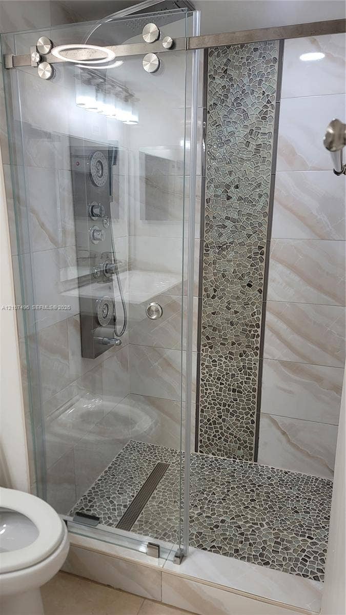 330 Racquet Club Road, #204, Weston, Weston, FL 33326 Walk-in shower featuring a sliding glass door, multi-jet shower panel, stone-tiled floor, and a decorative vertical stone mosaic inlay