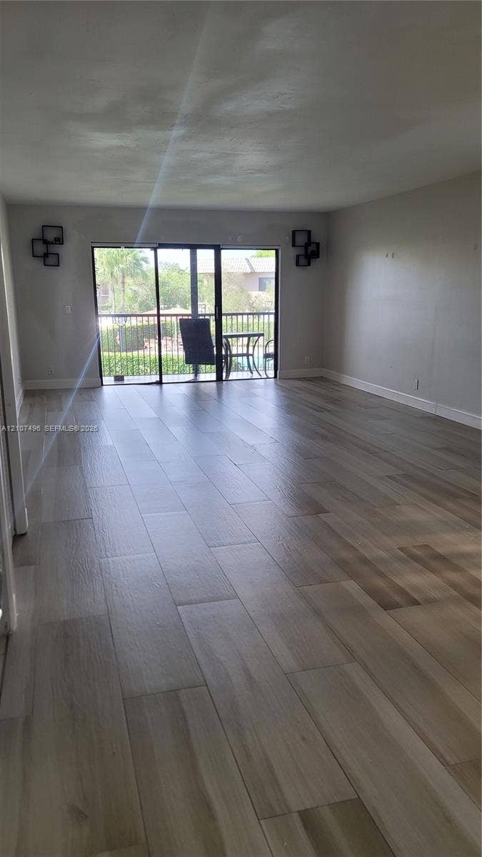 330 Racquet Club Road, #204, Weston, Weston, FL 33326 Open-concept living space featuring wood-finish flooring and sliding glass doors that provide access to a balcony with metal railing