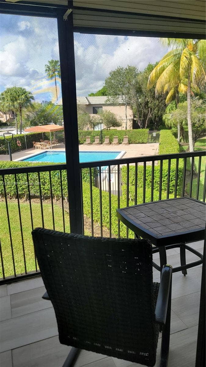 330 Racquet Club Road, #204, Weston, Weston, FL 33326 Screened balcony featuring metal railings and tile flooring, overlooking a community swimming pool, concrete deck, and perimeter hedges