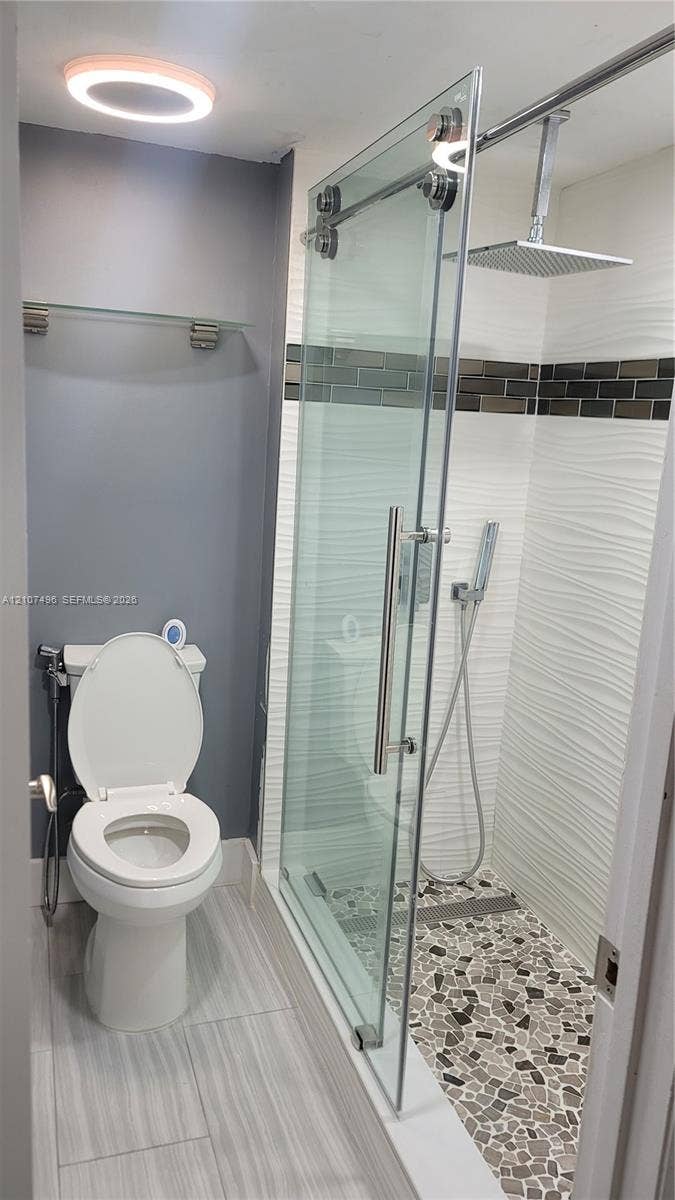 330 Racquet Club Road, #204, Weston, Weston, FL 33326 Walk-in shower featuring a pebble-style tile floor, glass sliding door, square rain shower head, and textured wall tile