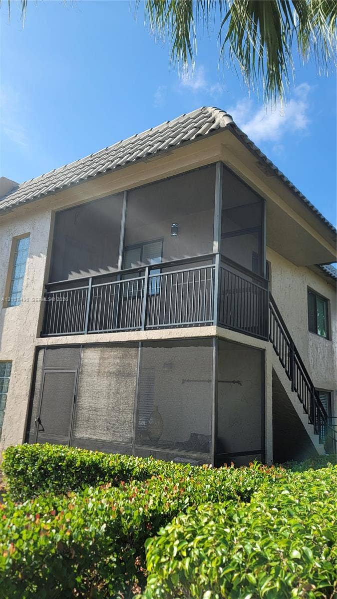 330 Racquet Club Road, #204, Weston, Weston, FL 33326 Two-story stucco exterior featuring stacked screened-in balconies, metal railings, and a tile roof