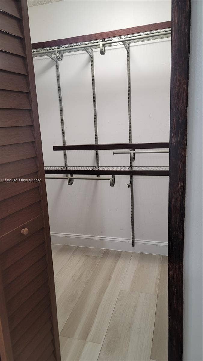 330 Racquet Club Road, #204, Weston, Weston, FL 33326 Walk-in closet featuring wood-finish flooring, louvered doors, and multi-tier wire shelving with integrated hanging rods
