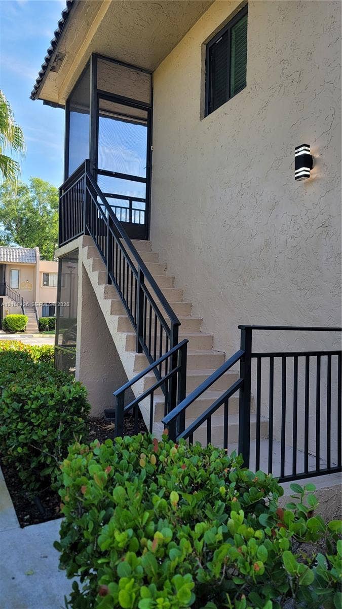 330 Racquet Club Road, #204, Weston, Weston, FL 33326 Exterior staircase with black metal railings, screened-in entry landing, stucco siding, and wall-mounted exterior lighting
