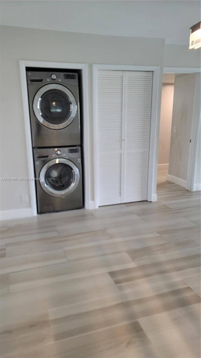 330 Racquet Club Road, #204, Weston, Weston, FL 33326 Stacked stainless steel laundry appliances and adjacent closet with white louvered doors, set against wood-finish flooring