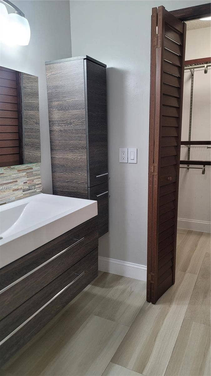 330 Racquet Club Road, #204, Weston, Weston, FL 33326 Floating dark wood-finish vanity with an integrated basin, vertical built-in cabinetry, multicolored tile backsplash, and bifold louvered wood doors