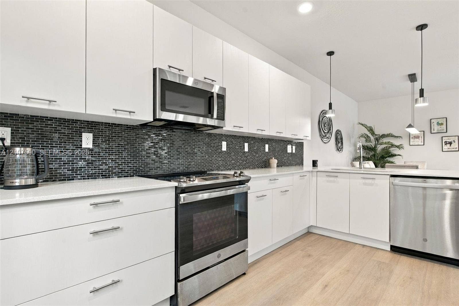 Kitchen featuring white flat-panel cabinetry, light-toned stone countertops, black mosaic tile backsplash, stainless steel appliances, and wood-finish flooring