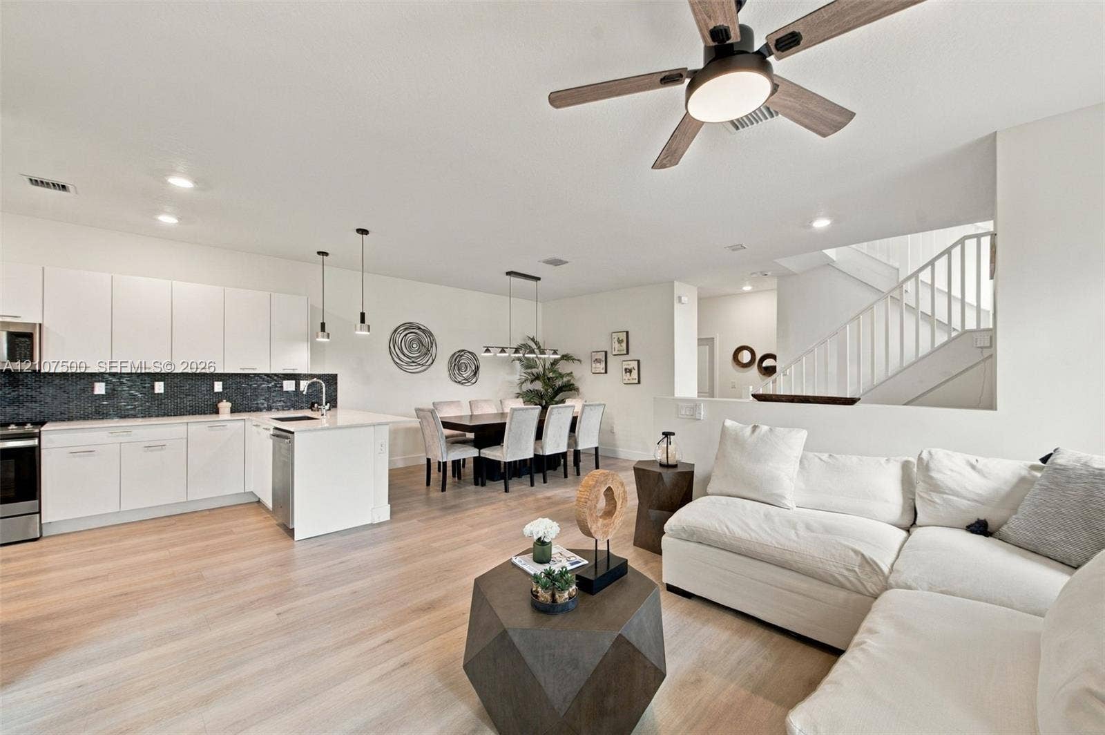 Kitchen featuring white flat-panel cabinetry, a dark tile backsplash, and a central island with countertop seating, complemented by wood-finish flooring, recessed lighting, and a modern ceiling fan