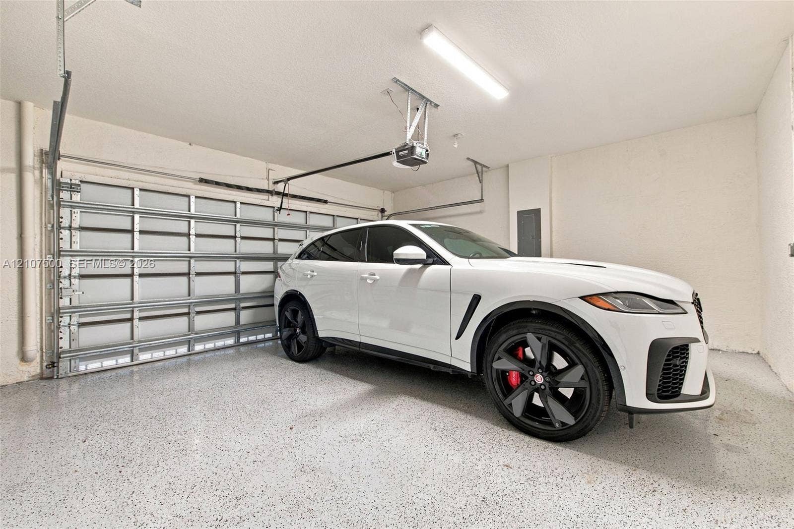 Enclosed garage featuring finished epoxy flooring, automated door mechanism, and overhead lighting