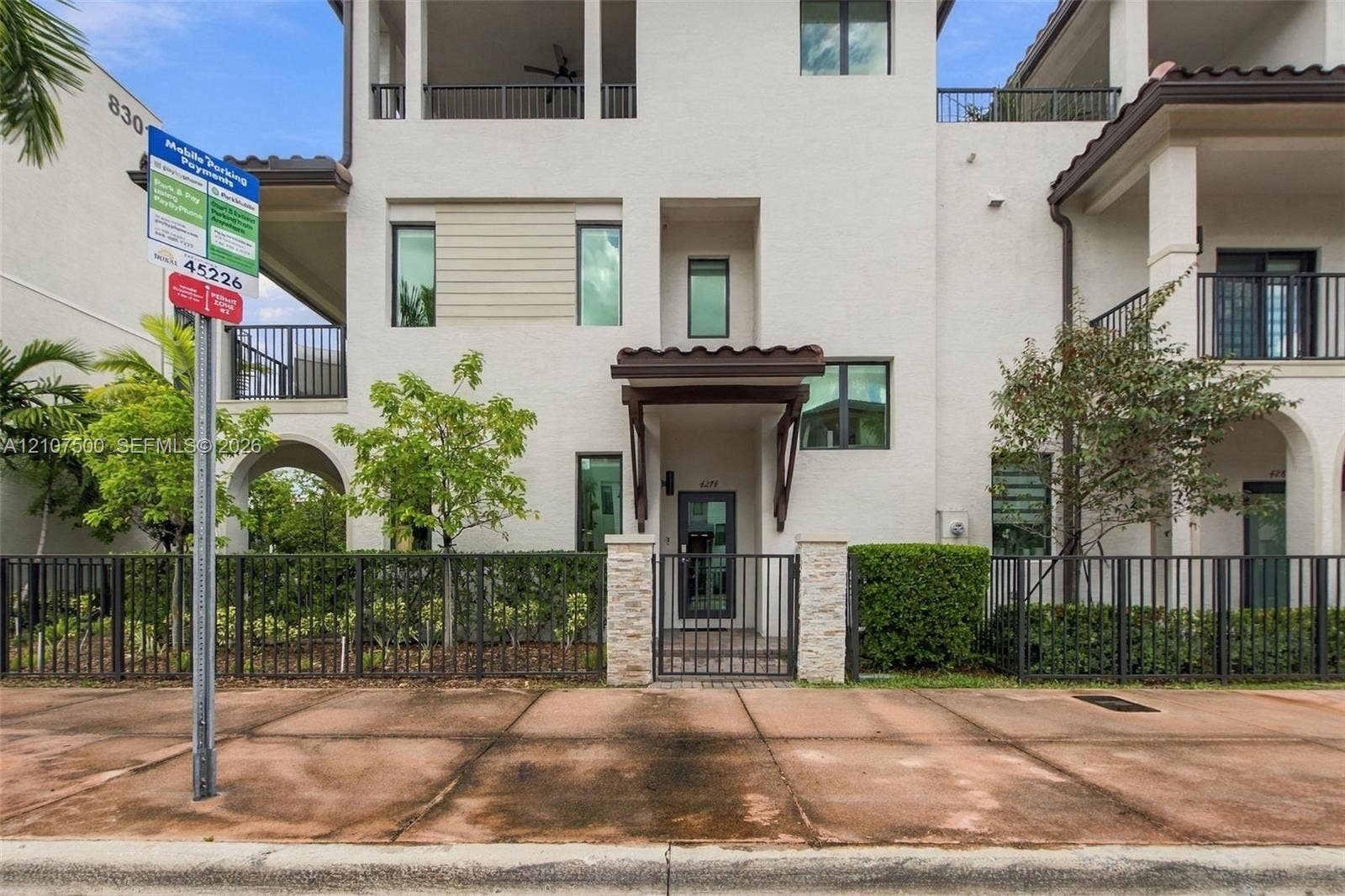 Stucco exterior featuring multi-level balconies, stone-accented entryway, tile roofing, and metal perimeter fencing