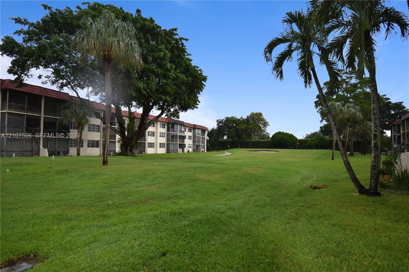 830 S Hollybrook Drive, #207, Pembroke Pines, FL 33025 Exterior of a multi-story building featuring screened balconies, expansive green space, mature canopy trees, and established palm trees