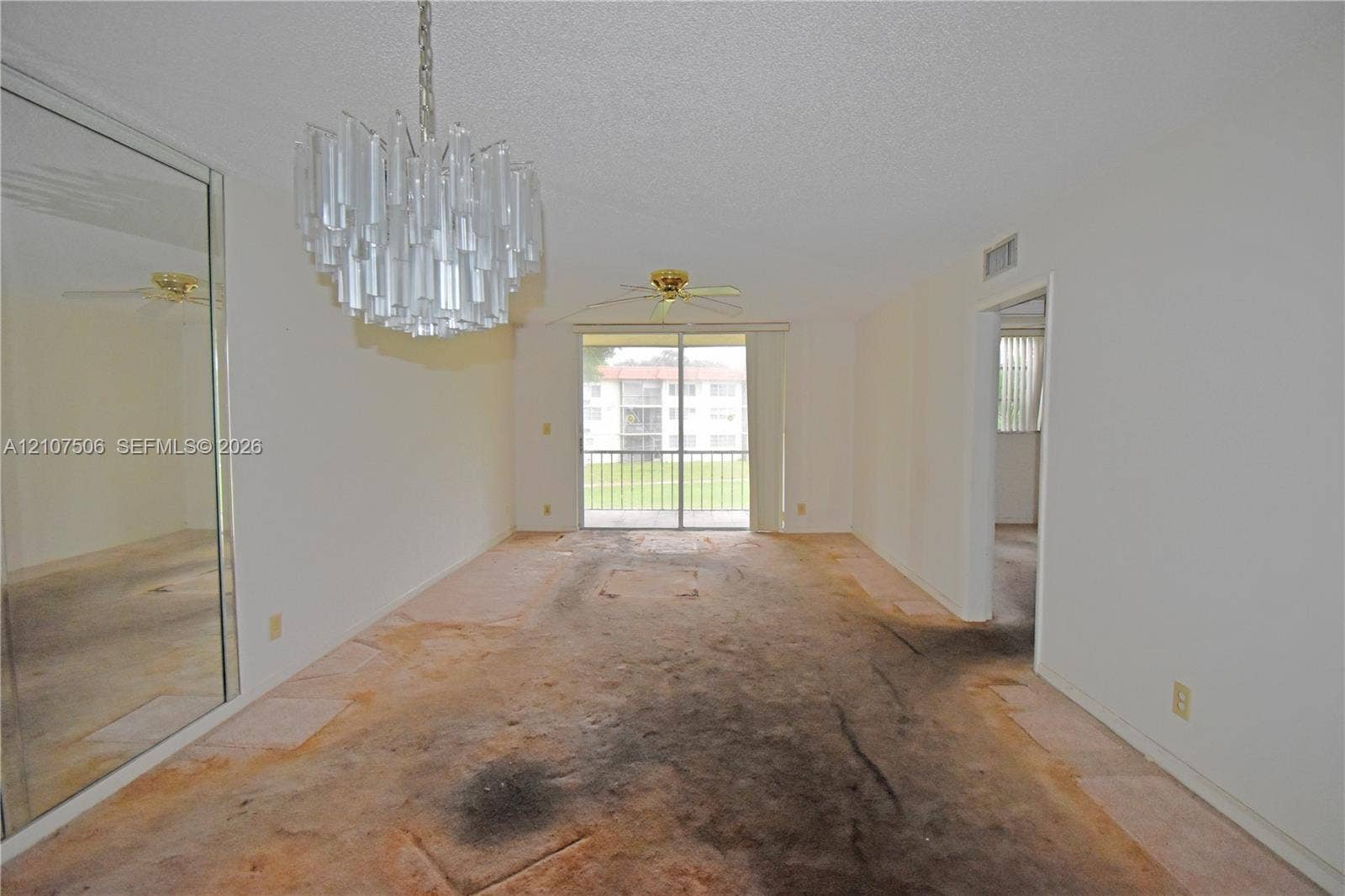 830 S Hollybrook Drive, #207, Pembroke Pines, FL 33025 Living area featuring a tiered glass chandelier, mirrored wall paneling, a ceiling fan, and sliding glass doors leading to a balcony