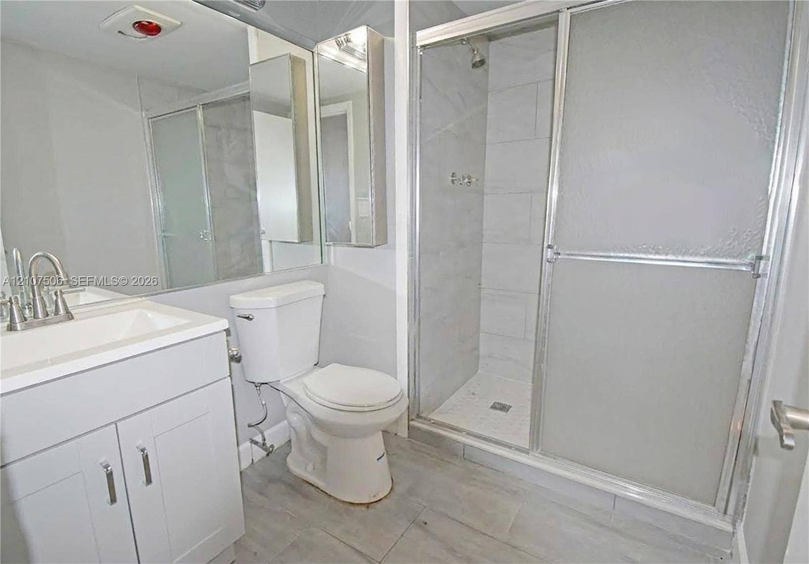 830 S Hollybrook Drive, #207, Pembroke Pines, FL 33025 Bathroom featuring a white vanity cabinet, rectangular under-mount sink, tile-surround shower with sliding glass doors, and large-format tile flooring