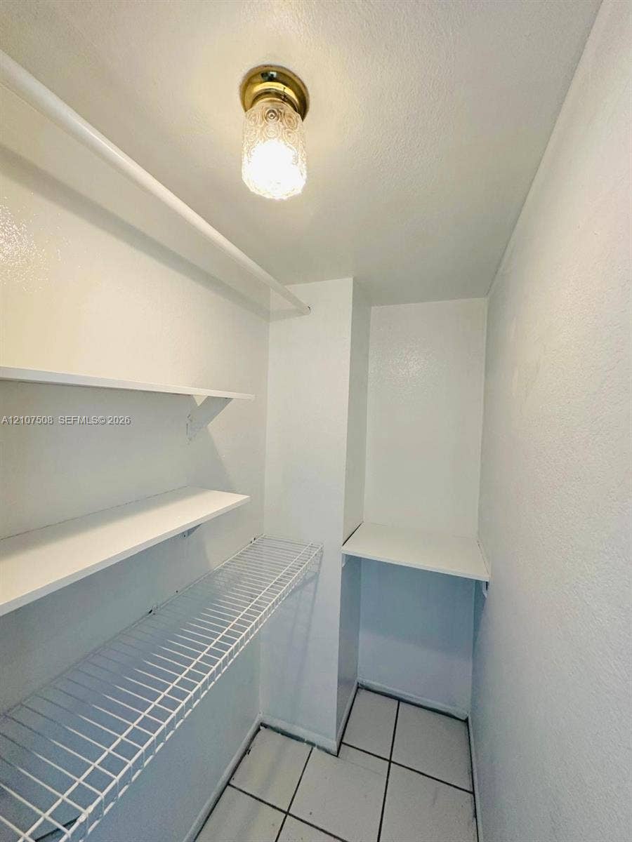 1020 Meridian Avenue, #415, Miami Beach, Miami Beach, FL 33139 Storage space featuring white solid shelving, white wire shelving, tile flooring, and a flush-mount brass-finish light fixture with textured glass