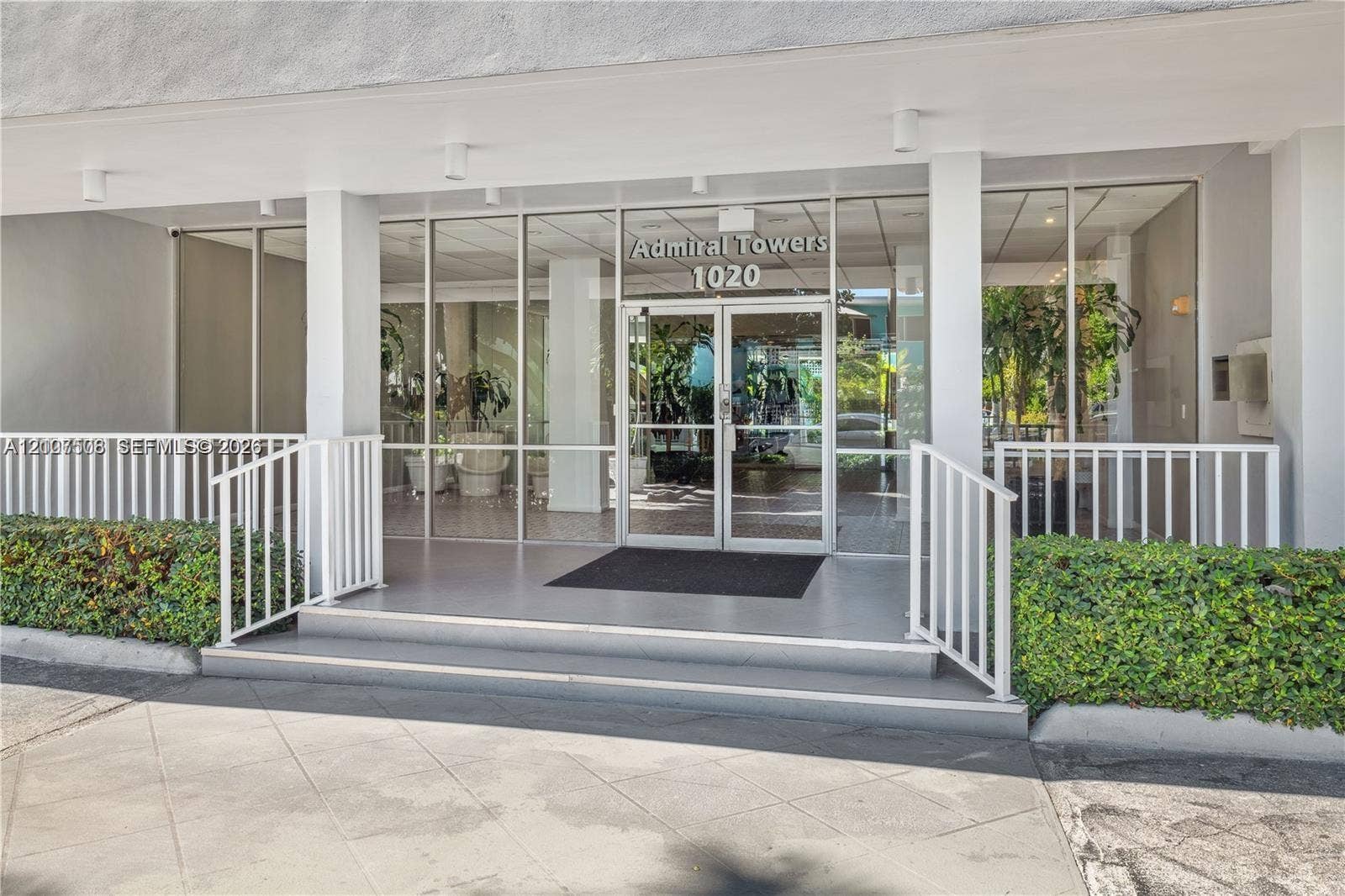1020 Meridian Avenue, #415, Miami Beach, Miami Beach, FL 33139 Building entrance featuring full-height glass paneled doors, expansive floor-to-ceiling windows, white metal railings, and a tiled walkway