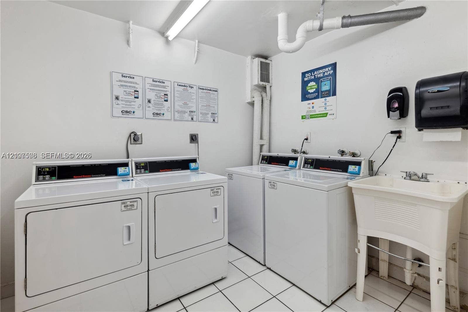 1020 Meridian Avenue, #415, Miami Beach, Miami Beach, FL 33139 Laundry facility featuring dual white coin-operated washers and dryers, a utility sink with a dual-handle faucet, and white ceramic tile flooring