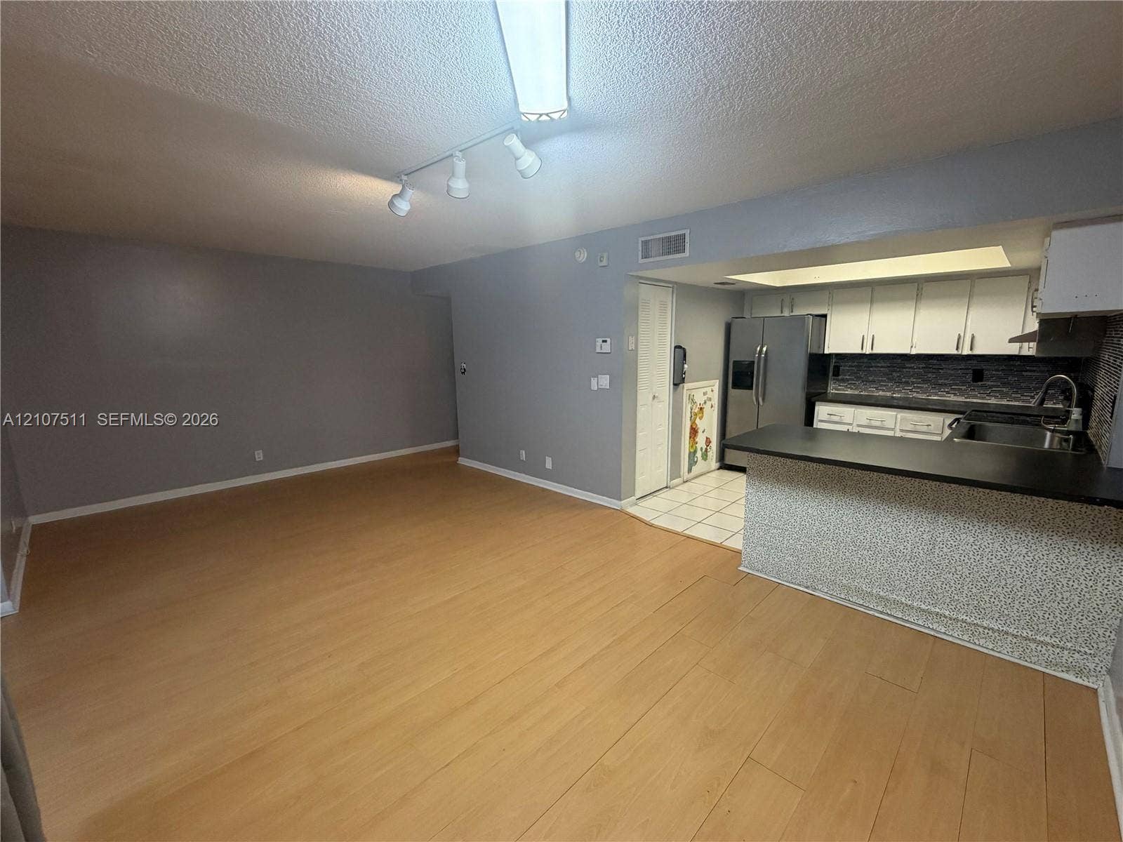 12 S Valencia Drive, #5-4, Davie, FL 33324 Open-concept area featuring wood-finish flooring, kitchen breakfast bar with solid-surface countertop, white cabinetry, stainless steel refrigerator, and track lighting