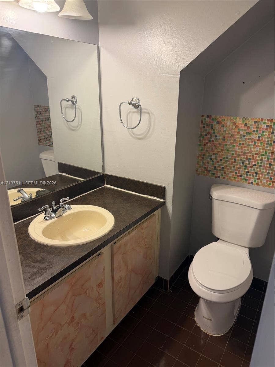 12 S Valencia Drive, #5-4, Davie, FL 33324 Bathroom featuring a vanity with dark countertop and integrated sink, full-width mirror, mosaic tile accents, and tiled flooring