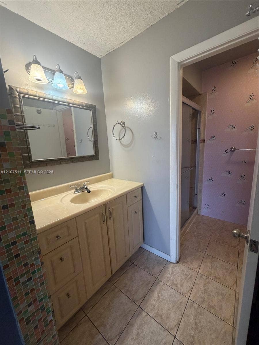 12 S Valencia Drive, #5-4, Davie, FL 33324 Bathroom featuring a vanity with integrated sink, ceramic tile flooring, multi-colored decorative tile wall accents, and a three-light vanity fixture