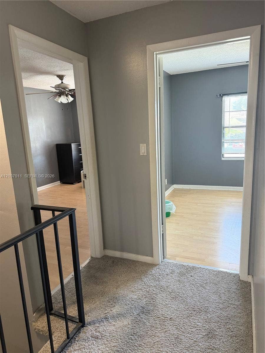 12 S Valencia Drive, #5-4, Davie, FL 33324 Interior hall featuring neutral-toned wall paint, wood-finish flooring in secondary rooms, carpeted hallway floor, and metal railing with vertical balusters