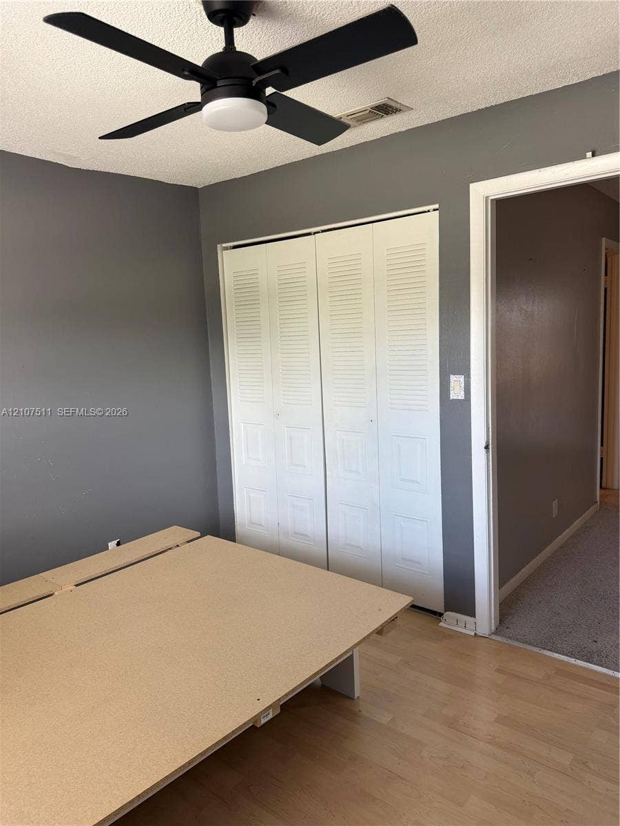 12 S Valencia Drive, #5-4, Davie, FL 33324 Neutral-toned walls paired with light wood-finish flooring, featuring a matte black ceiling fan with integrated lighting and bi-fold closet doors