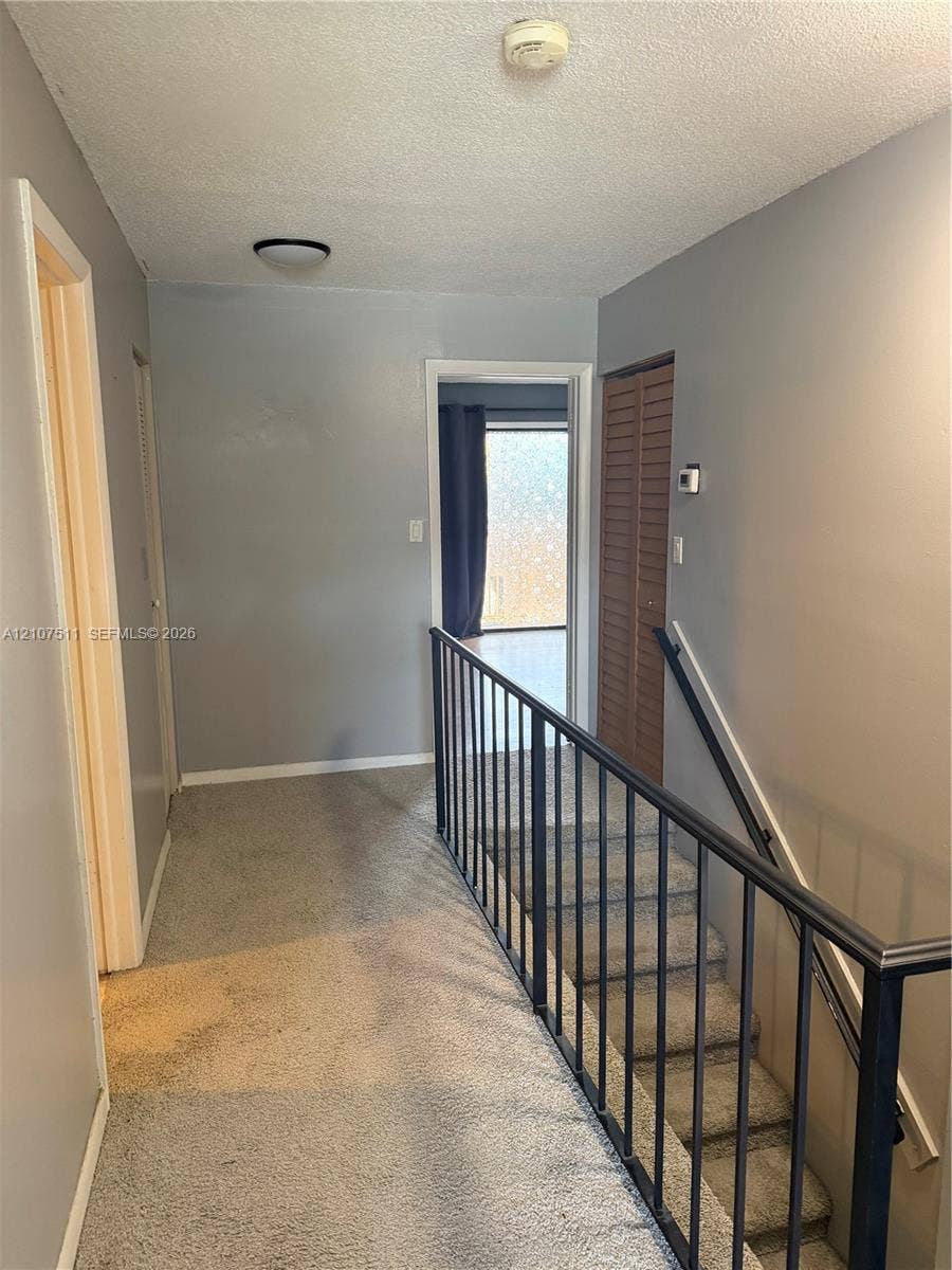 12 S Valencia Drive, #5-4, Davie, FL 33324 Hallway featuring neutral wall paint, carpeted flooring, and a staircase with a black metal railing
