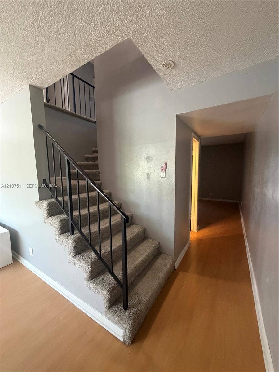 12 S Valencia Drive, #5-4, Davie, FL 33324 Staircase with carpeted treads and black metal railing, featuring wood-finish flooring and neutral-toned wall paint