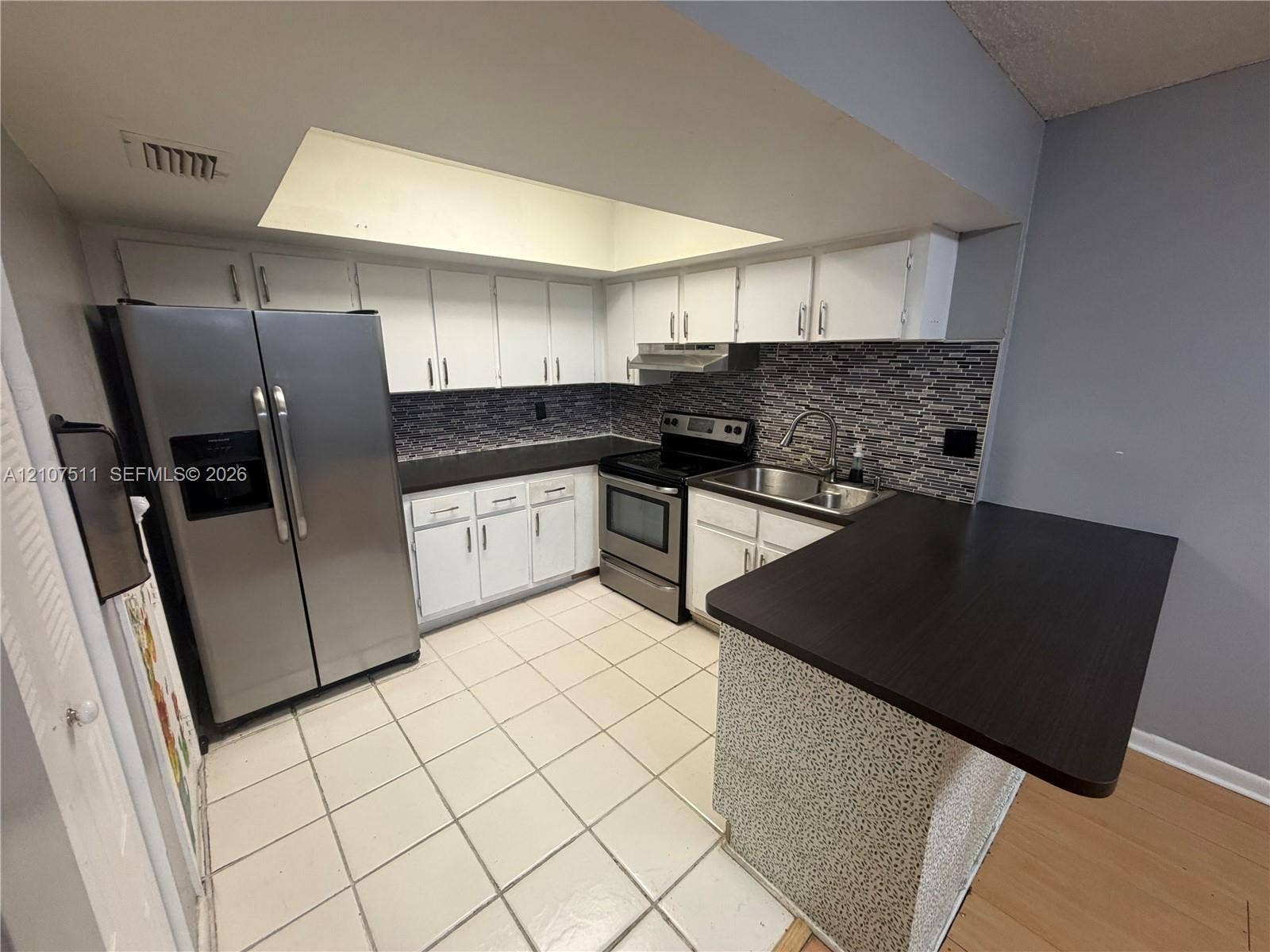 12 S Valencia Drive, #5-4, Davie, FL 33324 Kitchen featuring white cabinetry, stainless steel appliances, dark countertops, a stone-style tile backsplash, and a recessed ceiling light feature