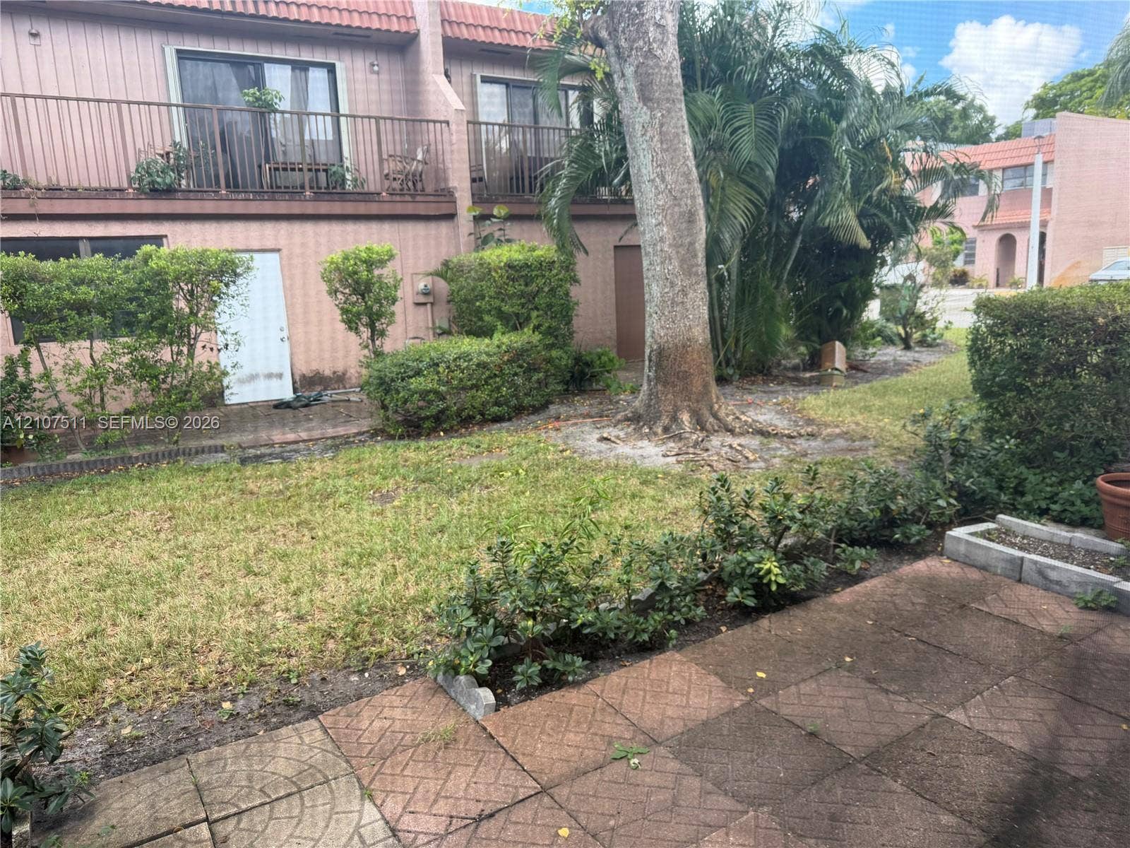12 S Valencia Drive, #5-4, Davie, FL 33324 Ground-level patio with paved hardscaping, landscaped lawn, mature trees, and second-story balcony