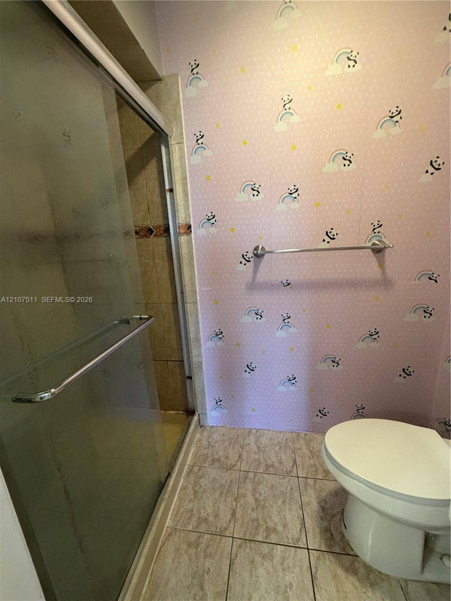 12 S Valencia Drive, #5-4, Davie, FL 33324 Shower enclosure with sliding glass doors, metal hardware, and tiled surround, featuring ceramic floor tile and a wall-mounted metal towel bar