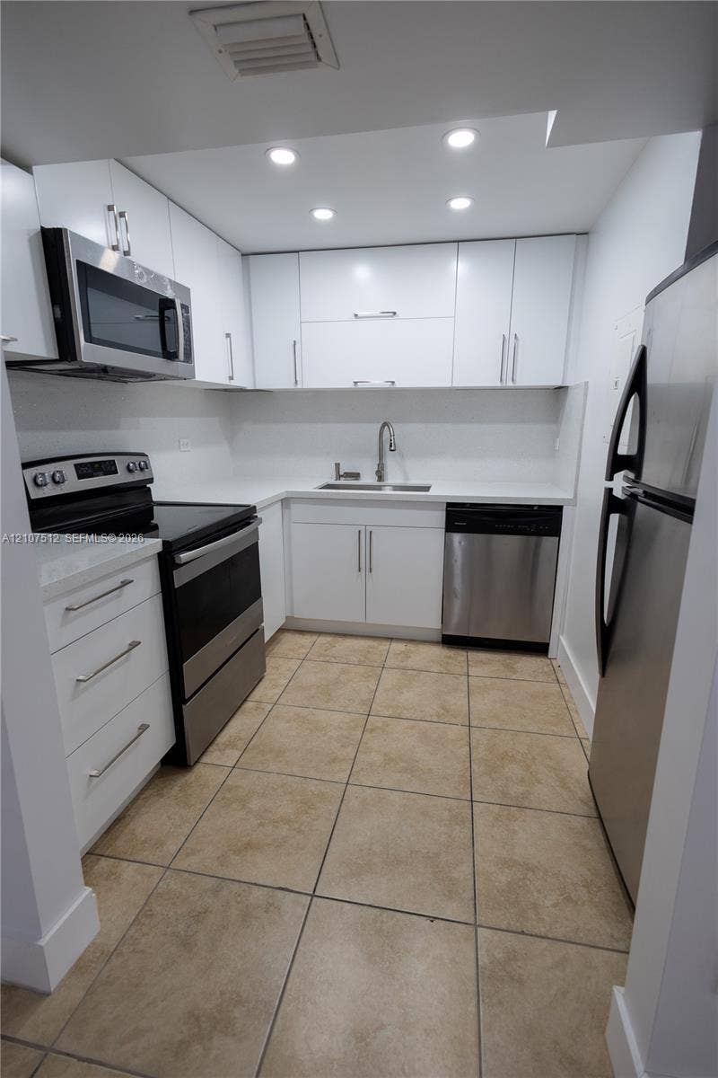 1720 N River Drive, #302, Miami, FL 33125 Kitchen featuring white cabinetry with brushed-metal pulls, stone-finish countertops, stainless steel appliances, and tile flooring