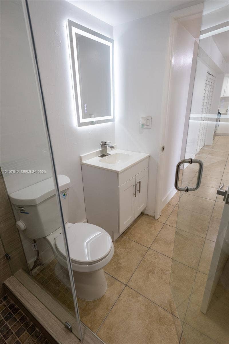 1720 N River Drive, #302, Miami, FL 33125 Bathroom featuring a vanity with a solid-surface countertop, an integrated sink, a frameless glass shower enclosure, a LED-backlit mirror, and tile flooring