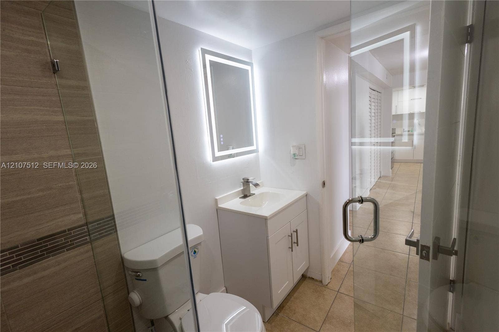 1720 N River Drive, #302, Miami, FL 33125 Bathroom featuring a glass-enclosed shower with tiled walls, an illuminated vanity mirror, a white cabinet vanity with a sink, and ceramic tile flooring