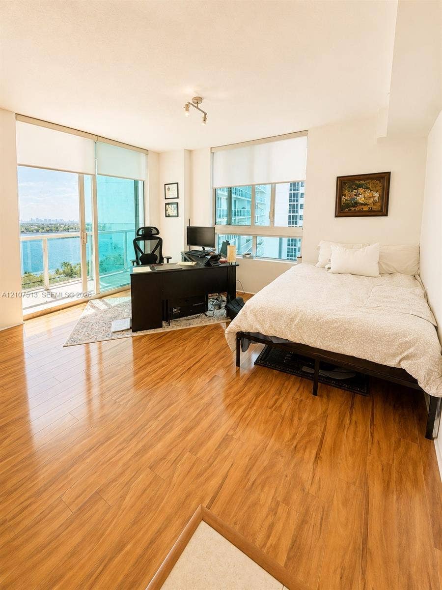 1900 N Bayshore Drive, #3005, Miami, FL 33132 Wood-finish flooring, floor-to-ceiling glass sliding doors, window roller shades, and a glass-paneled balcony railing with water scenery
