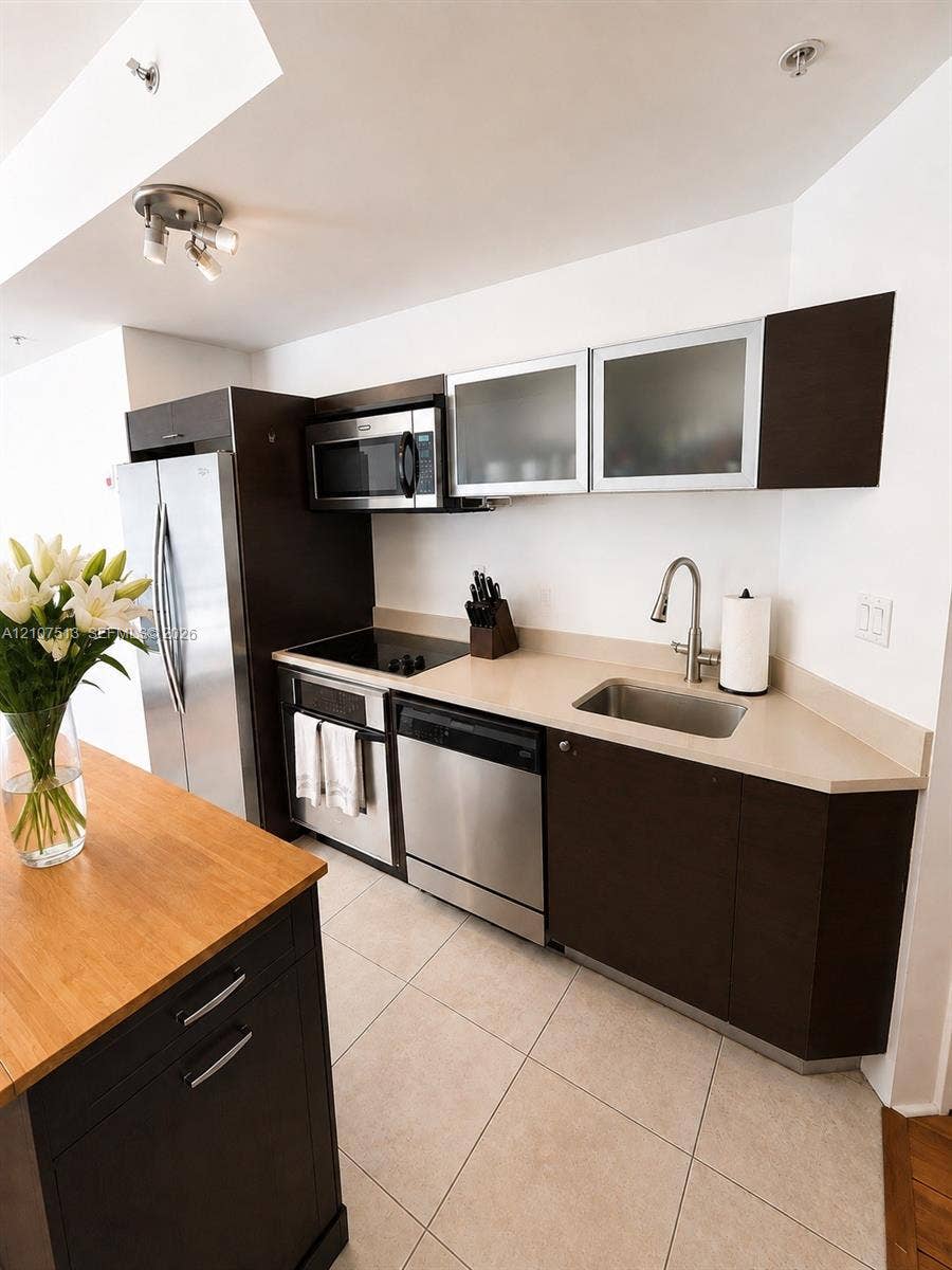 1900 N Bayshore Drive, #3005, Miami, FL 33132 Kitchen featuring dark-finish cabinetry, stainless steel appliances, neutral stone-finish countertops, ceramic tile flooring, and an island with a wood-finish top