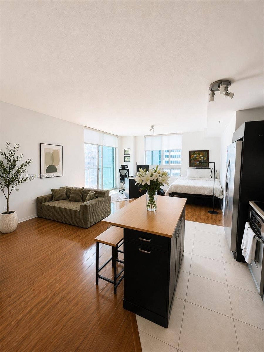 1900 N Bayshore Drive, #3005, Miami, FL 33132 Open-concept interior featuring wood-finish flooring, tile kitchen flooring, a central island with a wood countertop, large-pane glass balcony doors, and track lighting
