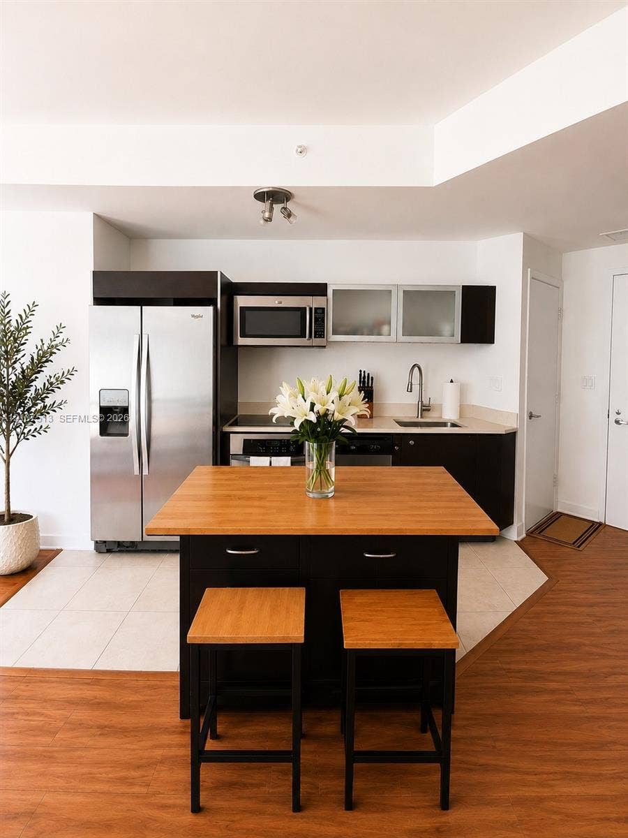 1900 N Bayshore Drive, #3005, Miami, FL 33132 Kitchen featuring stainless steel appliances, dark cabinetry, frosted glass cabinet doors, wood-finish countertop on center island, and wood-finish flooring