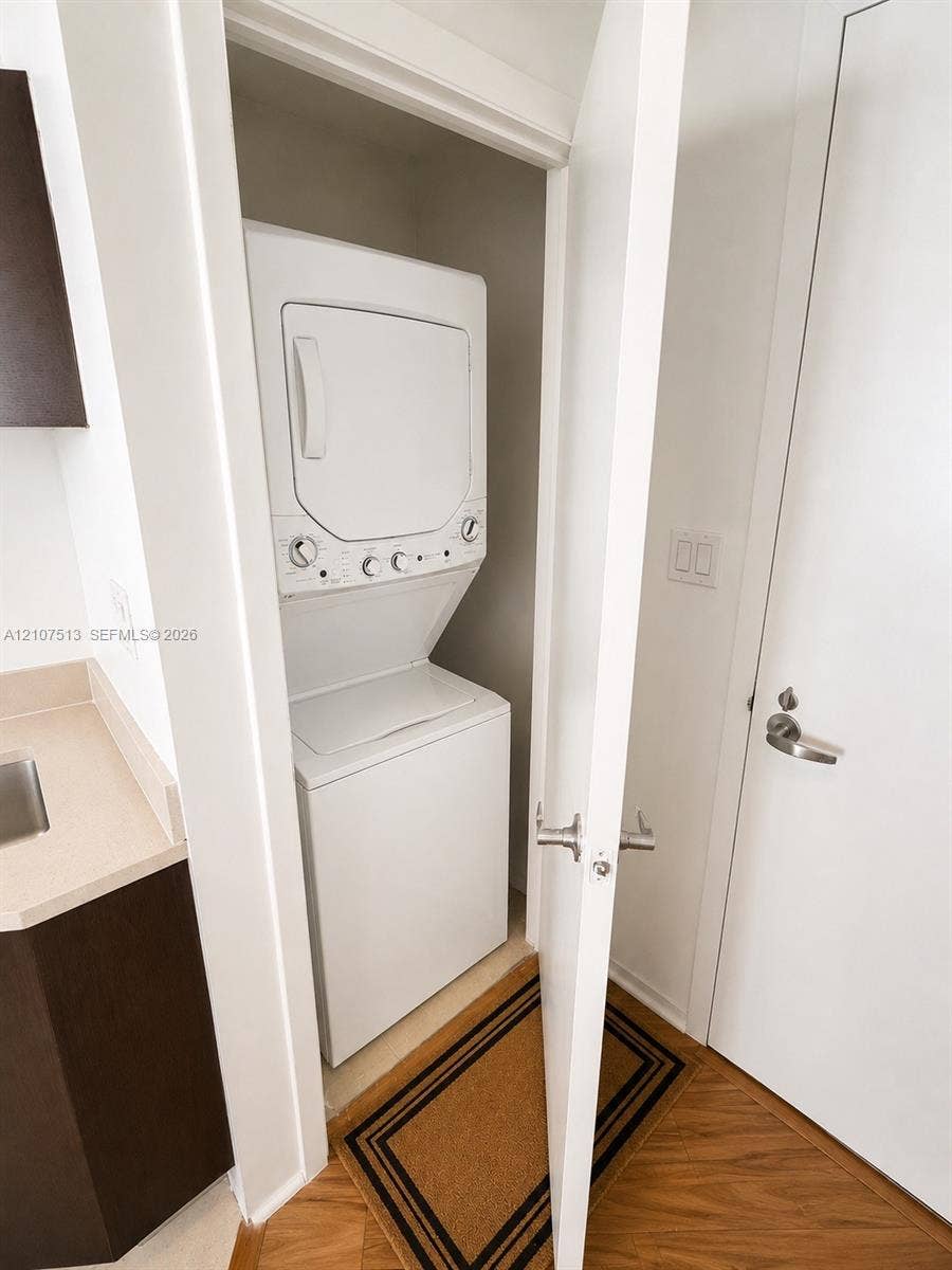 1900 N Bayshore Drive, #3005, Miami, FL 33132 Stacked laundry center with white finish, integrated cabinetry with solid-surface countertop, and wood-finish flooring