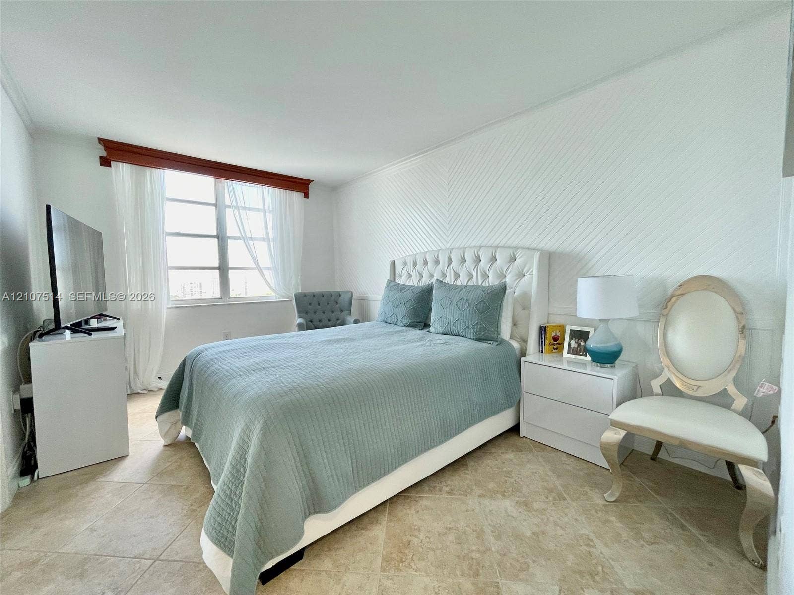 2750 NE 183rd Street, #2310, Aventura, Aventura, FL 33160 Bedroom featuring neutral tile flooring, herringbone-patterned wall paneling, and a large multi-pane window with a wood-finish valance